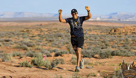 A man raises his arm in triumph as he runs on a desert course