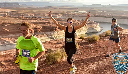 A man and two women are wearing racing bibs, running alongside a canyon in a race.